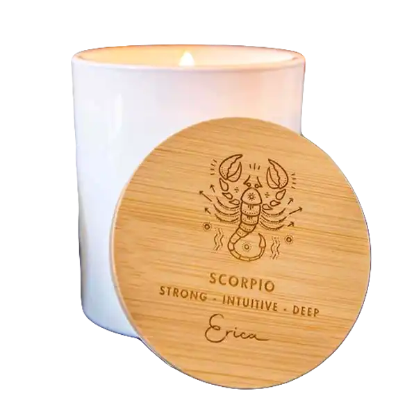 A white jar candle topped with a bamboo lid engraved with the Scorpio zodiac symbol and personalized text, set in a cozy scene