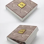White Ramadan gift box featuring a layered arched-line pattern in brown, opened to display an assortment of luxury dates