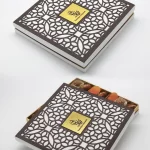 White Ramadan box with a dark brown lattice-cut lid, opened to show dried apricots and premium dates inside