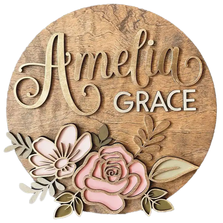 A round wooden plaque showcasing the name ‘Amelia Grace’ in layered lettering, accented by 3D floral cutouts in soft pink and green.