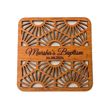 A square laser-cut wooden coaster with sunburst cutouts, personalized with ‘Marsha’s Baptism’ and a date beneath