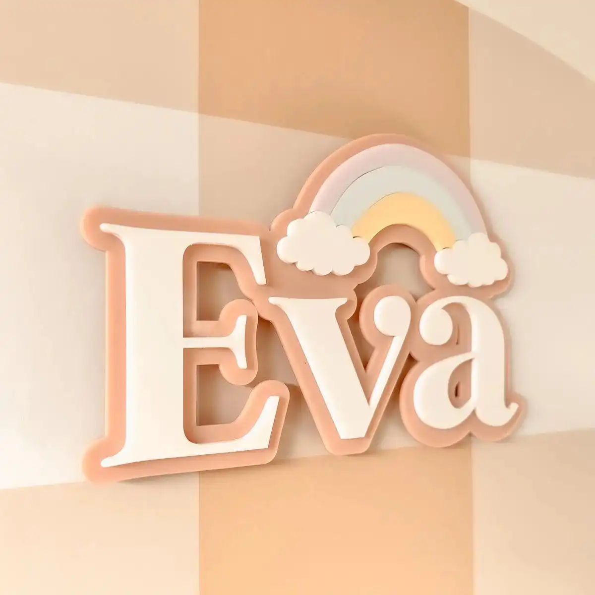 A pastel-colored name sign with layered lettering spelling ‘Eva,’ decorated with a rainbow and fluffy cloud shapes.