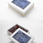 White gift box featuring a 3D layered navy-blue Ramadan motif, opened to reveal premium dates underneath