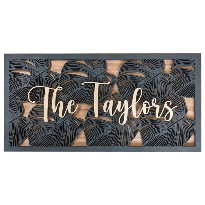 A rectangular wooden sign with laser-cut tropical leaf motifs and the family name ‘The Taylors’ in cursive lettering