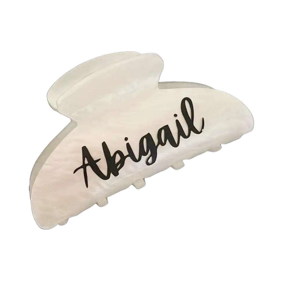 A pearly white hair claw engraved with the name Abigail against a dark background. Gifts for Women