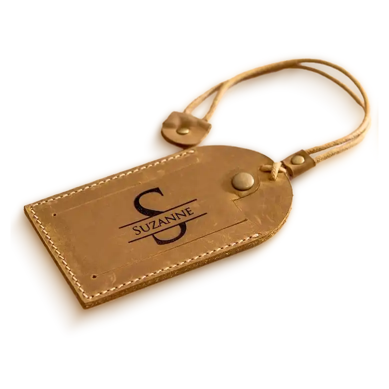 A brown leather luggage tag embossed with a large ‘S’ and the name Suzanne, placed on a marble surface.