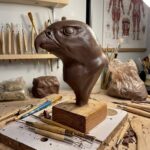 Detailed clay bust of an eagle head on a wooden stand surrounded by various carving and sculpting tools