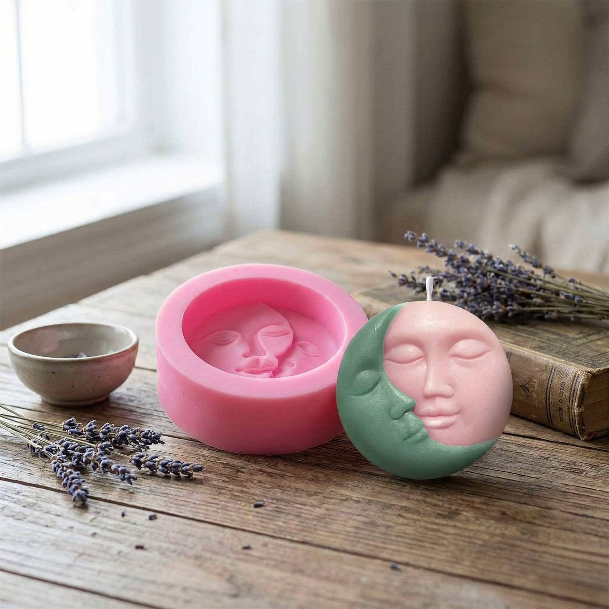 Pink silicone mold next to a finished two-toned moon face candle on a rustic wooden table.