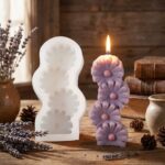 White silicone mold next to a lit purple candle shaped like stacked daisy flowers on a wooden table.