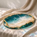 Oval colored epoxy resin serving tray with gold handles featuring a 3D ocean wave beach scene and a textured gold rim.