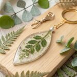 Leaf-shaped clear casting resin keychain perfectly encapsulating a bright green fern leaf and subtle glitter.