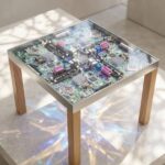 A square side table featuring a metal frame and wood legs with a surface made entirely of clear epoxy resin encapsulating a complex computer circuit board.