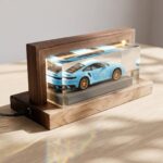 Light blue die-cast toy car encapsulated in a flawless clear epoxy resin block displayed inside an illuminated wooden frame.