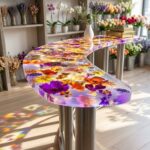 A curved, modern bar top made entirely of clear epoxy resin encapsulating a dense layer of colorful preserved flowers in a retail shop.