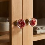 Round clear epoxy resin cabinet knobs encapsulating vibrant red dried flowers attached to a light wood cabinet door.