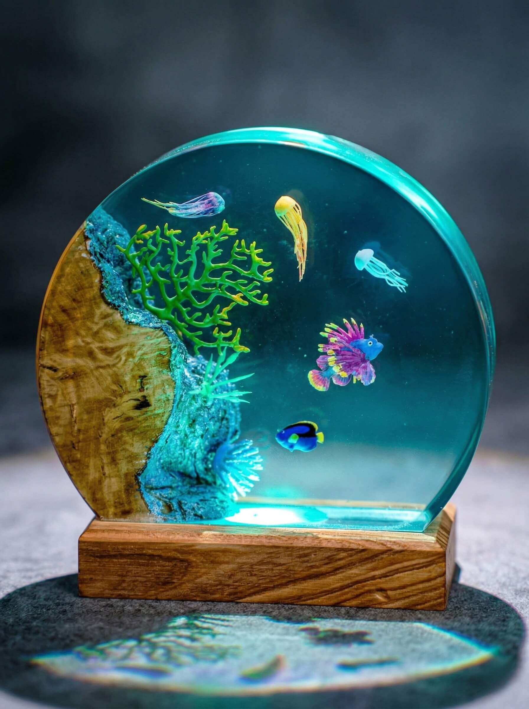 Round clear epoxy resin diorama on a wood base encapsulating a miniature underwater coral reef scene with tiny fish and jellyfish.