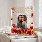 Thick clear epoxy resin block encapsulating a printed photograph of two women surrounded by red and yellow preserved flowers and gold flakes.