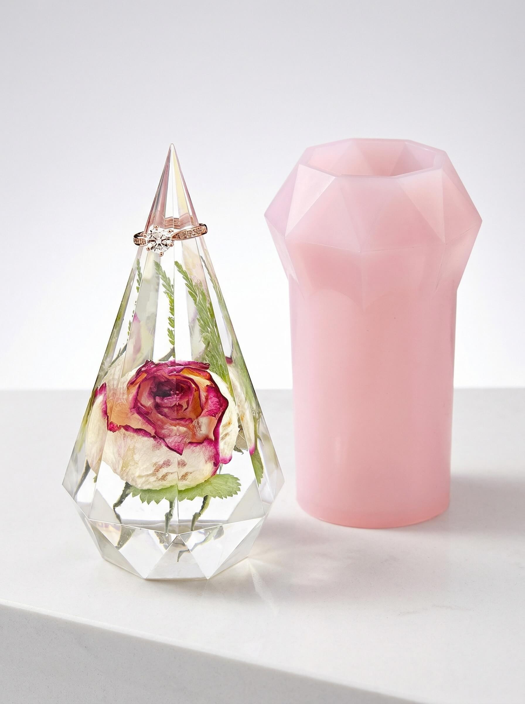 Faceted clear epoxy resin ring holder encapsulating a single preserved rose next to a pink silicone mold.