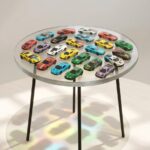 Round modern side table featuring a clear epoxy resin top encapsulating a large collection of colorful miniature toy cars.