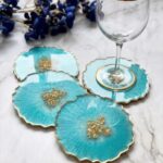 Set of three scalloped turquoise colored epoxy resin coasters featuring gold flake centers next to a wine glass.