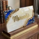 Freestanding geode style custom colored epoxy resin nameplate in pearlescent white and deep blue with crushed gold texture and raised gold lettering on a wooden base.