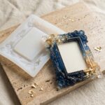 Ornate custom-cast colored epoxy resin photo frame in deep blue and gold resting next to its detailed silicone mold on a stone surface.