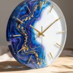 Modern round wall clock featuring a half-white face and half swirling deep blue and purple colored epoxy resin with gold flakes