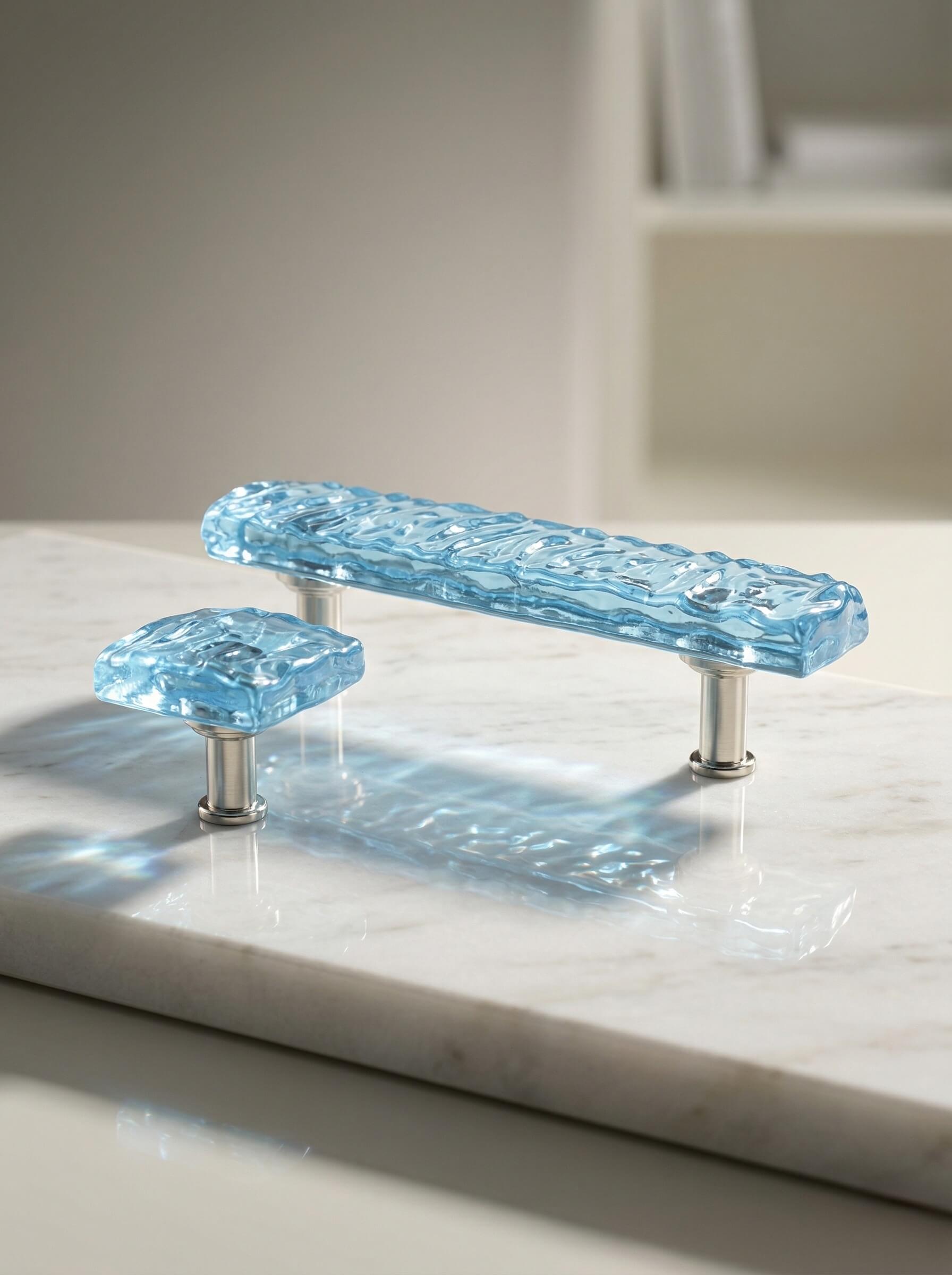 A rectangular drawer pull and matching square knob made of translucent blue textured epoxy resin on silver hardware.