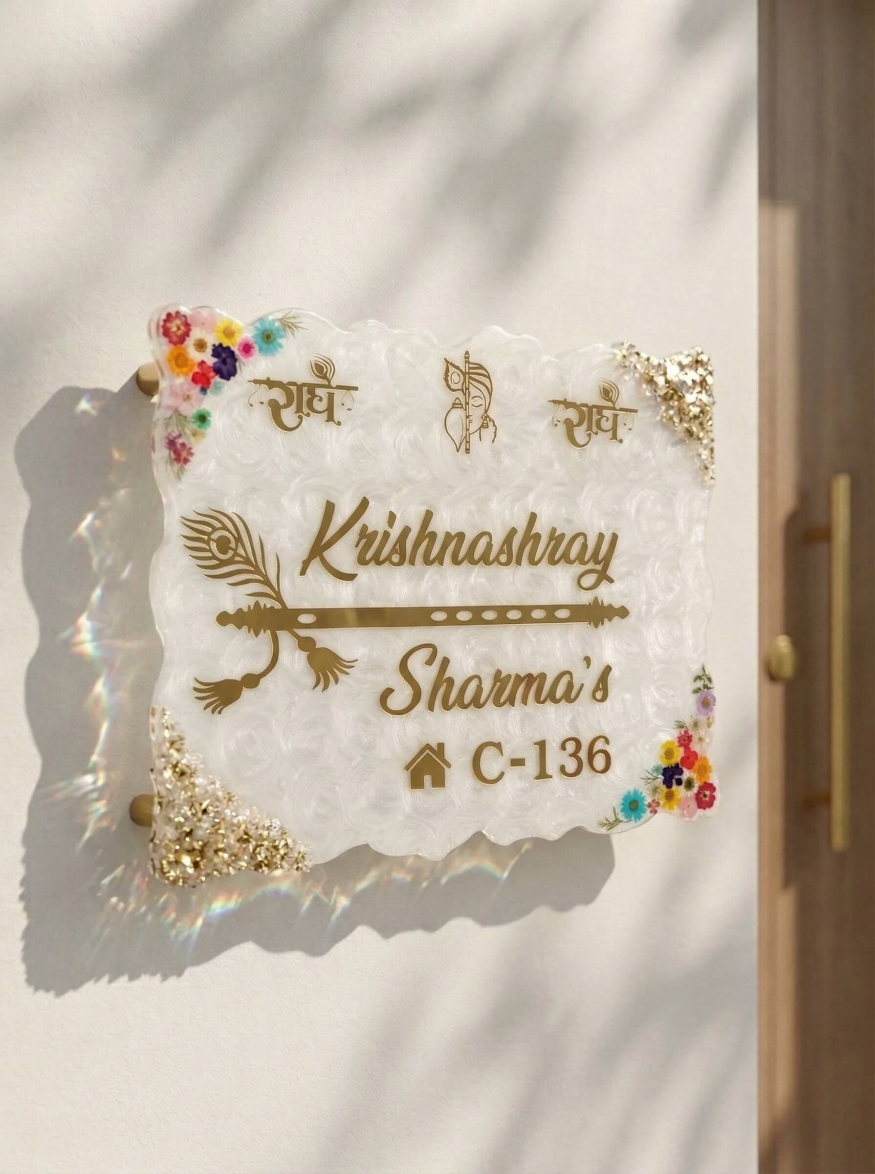 Custom white textured epoxy resin house address plate with gold lettering, encapsulated colorful flowers, and gold flakes mounted on an exterior wall.