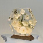 Hexagon-shaped clear casting resin block encapsulating preserved white roses and delicate greenery on a dark wood base.