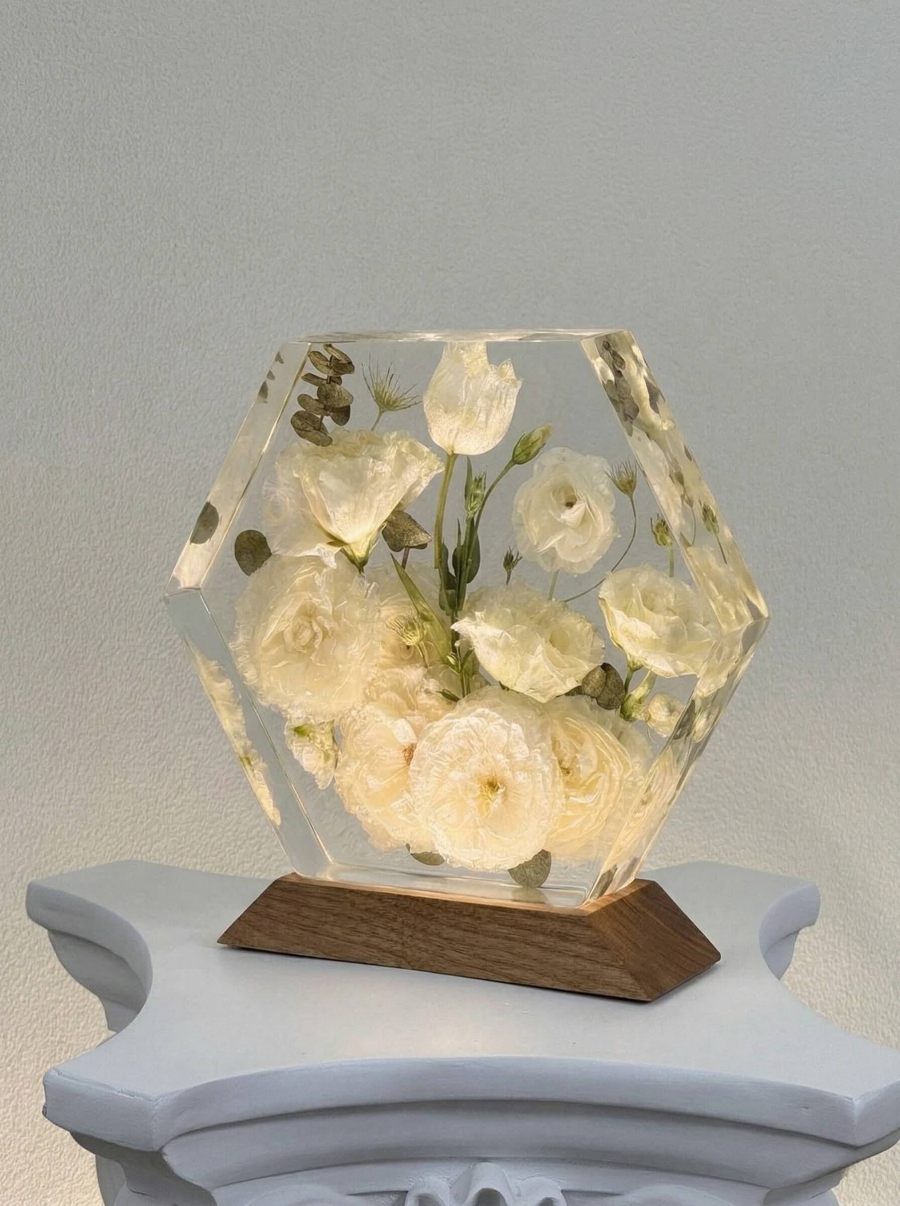 Hexagon-shaped clear casting resin block encapsulating preserved white roses and delicate greenery on a dark wood base.