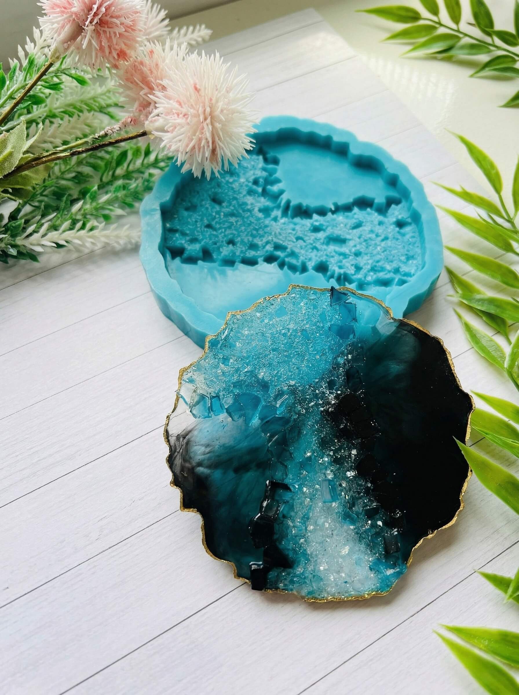 Textured geode style colored resin coaster in black, teal, and clear with gold edges next to a detailed silicone mold.